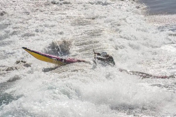 Seekajakfahrerin von der Seite, durch eine Welle fahrend.