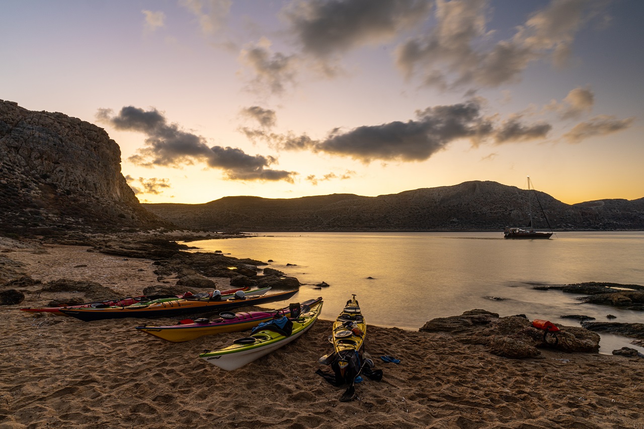 Blick vom Strand in der Abenddämmerung in eine Bucht mit Seekajaks im Vordergrund
